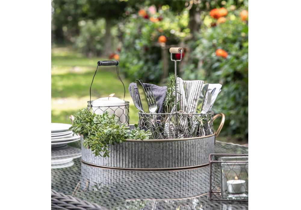 Small Garden Ideas - A silver galvanised metal tray with gold handles filled with cutlery, a candle and plant on a rattan table in a lawned garden
