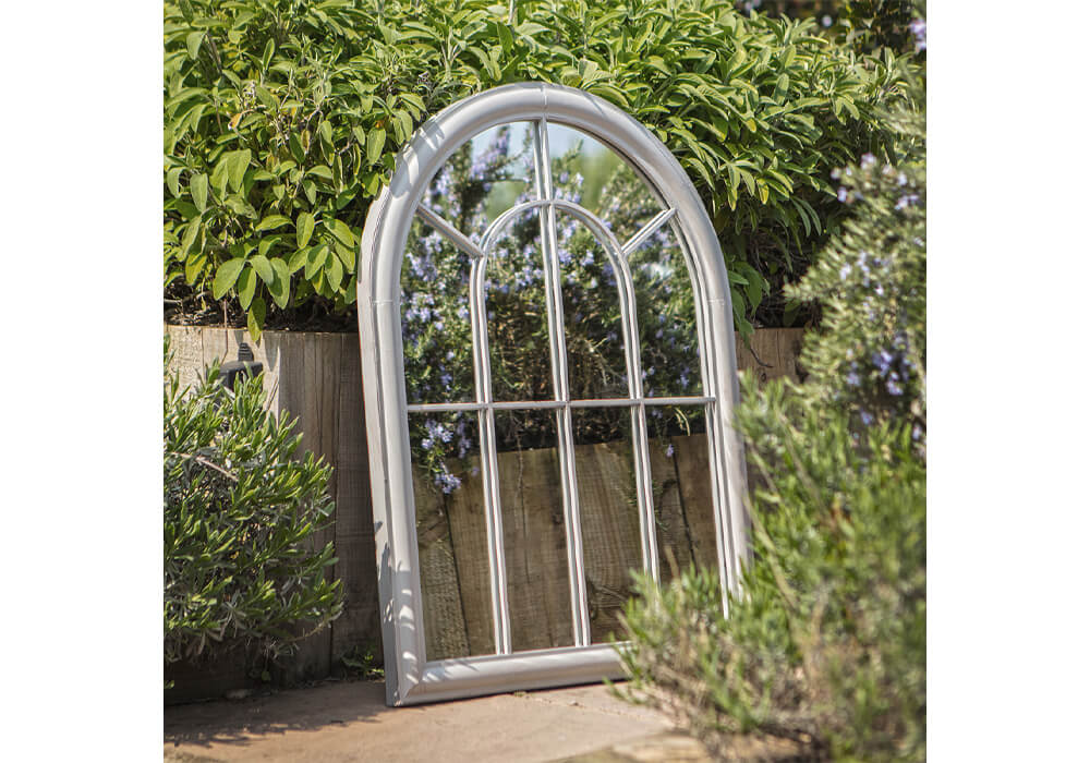 Small Garden Ideas - A large silver-framed mirror in arched window style among a rustic garden with leafy green shrubs